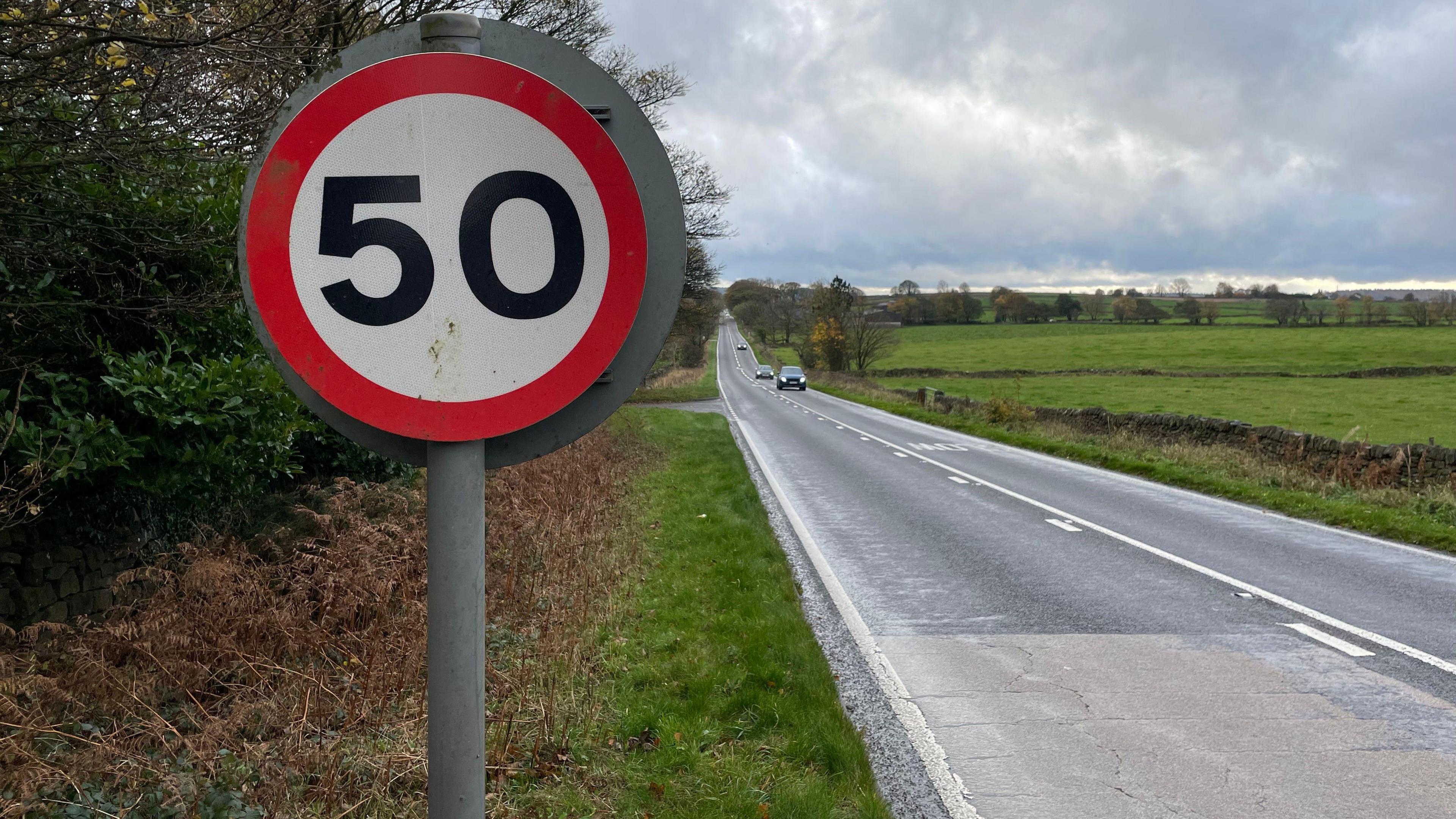 A long straight single-carriageway road with a 50mph sign in the foreground