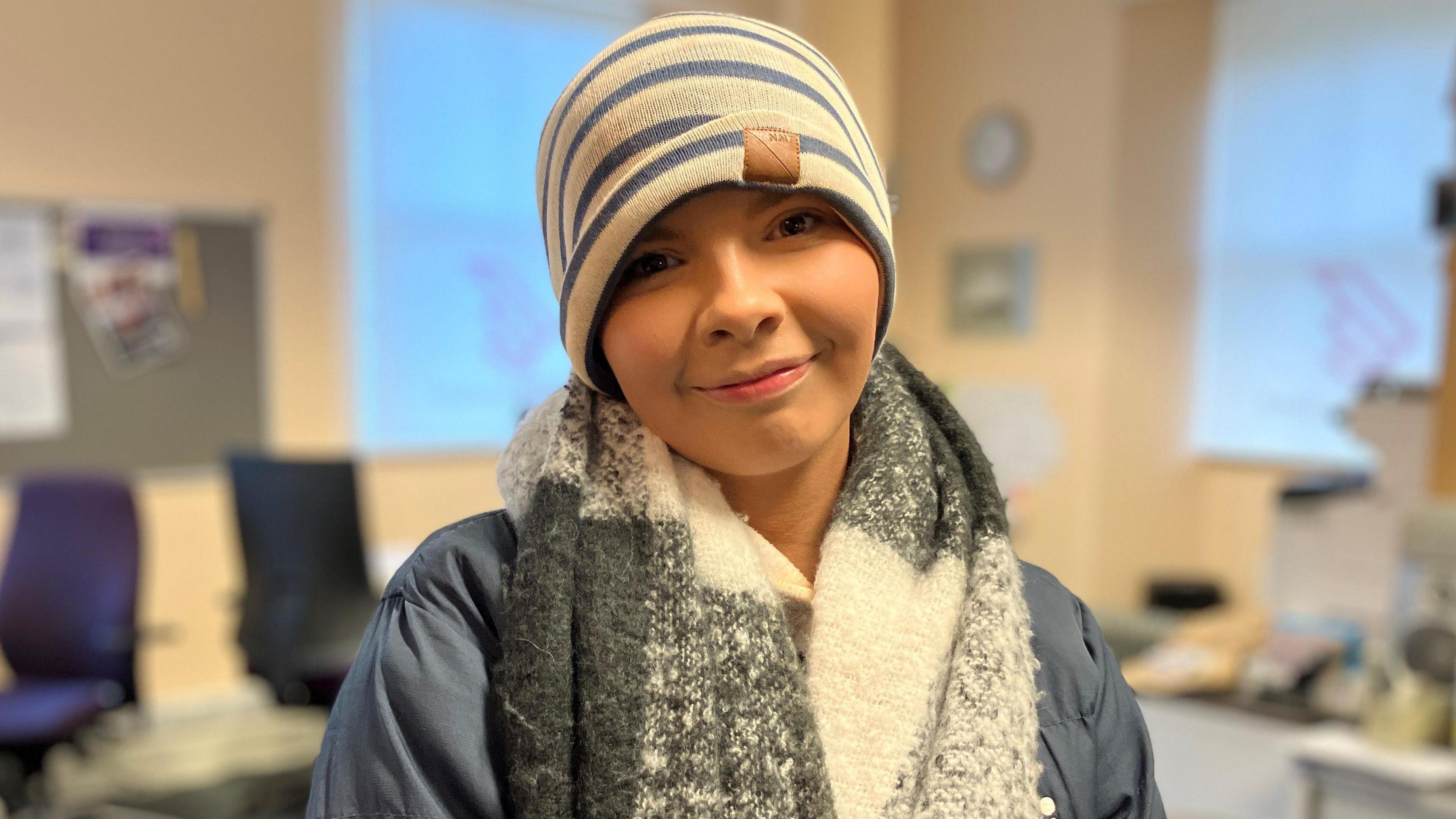 Jenny Thomson smiles at the camera, she is wearing a blue and white striped beanie hat and a fluffy scarf