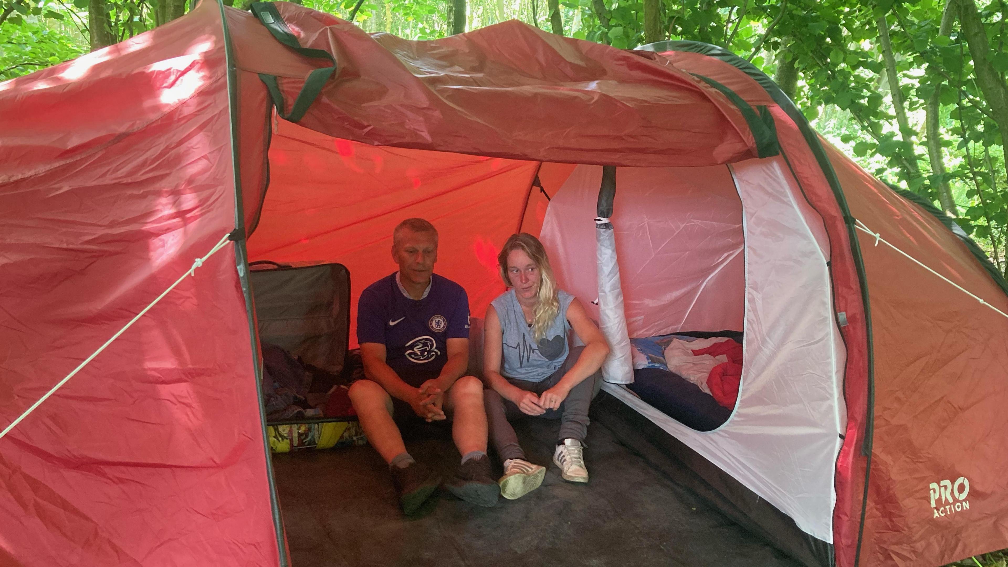 Man and woman sitting in a red tent in a woodland