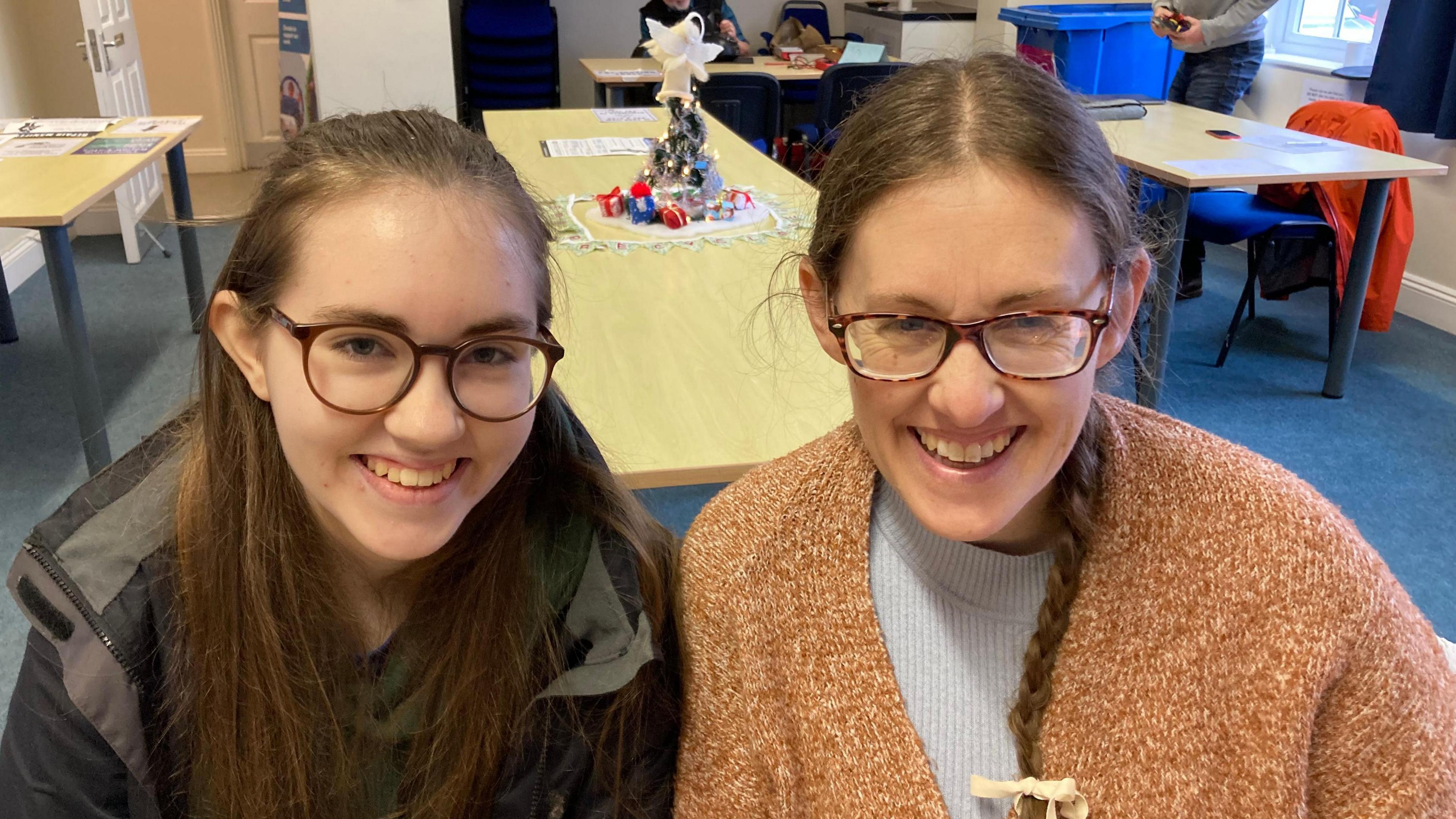 Rhiannon has long dark hair and glasses and wears a dark coat on the left - her mother Genny next to her wears a woolly cardigan and glasses