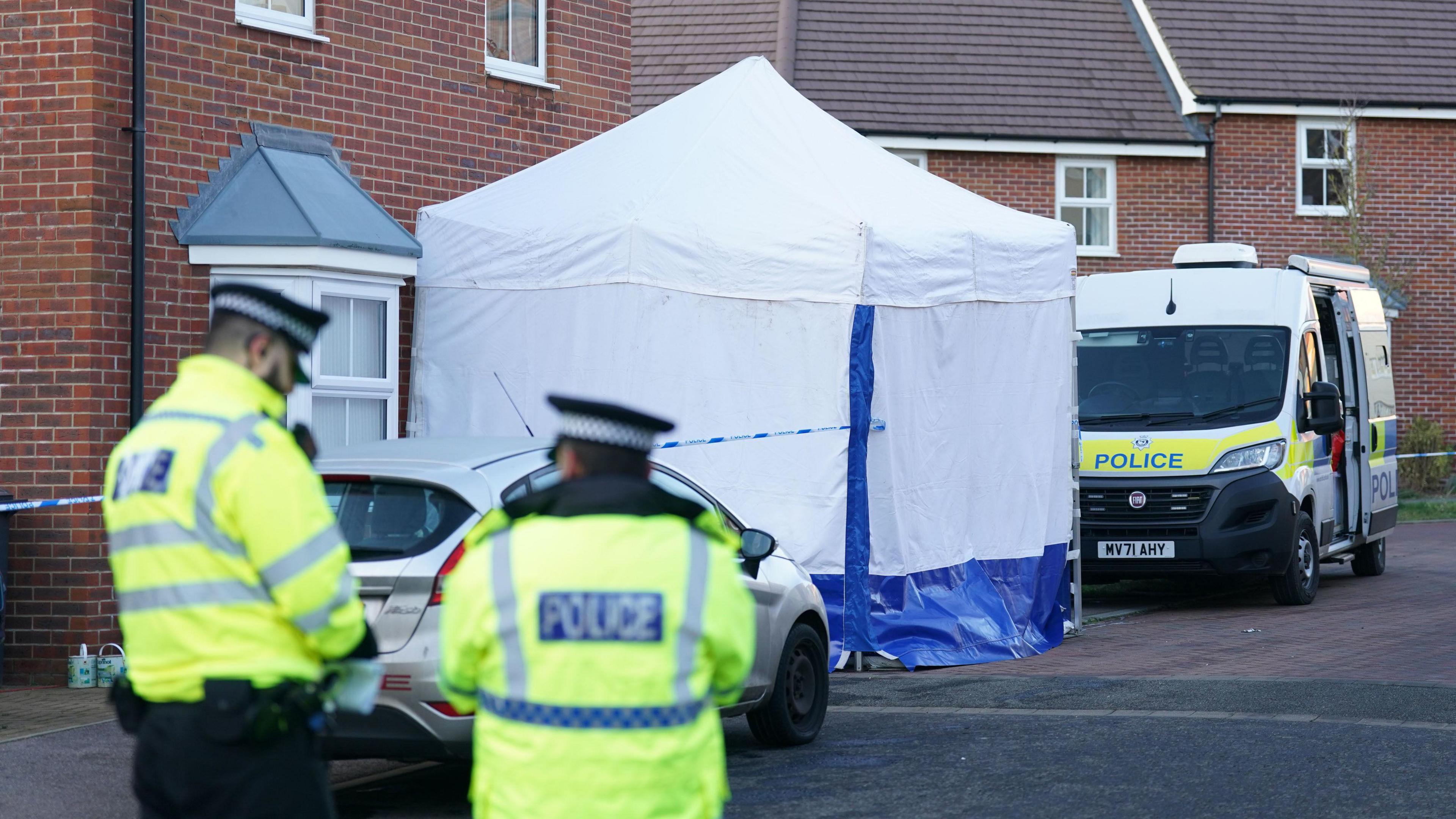 Two police officers stand down a road which has been cordoned off with blue and white police tape. A white tent has been put up on Allan Bedford Crescent in Costessey. 