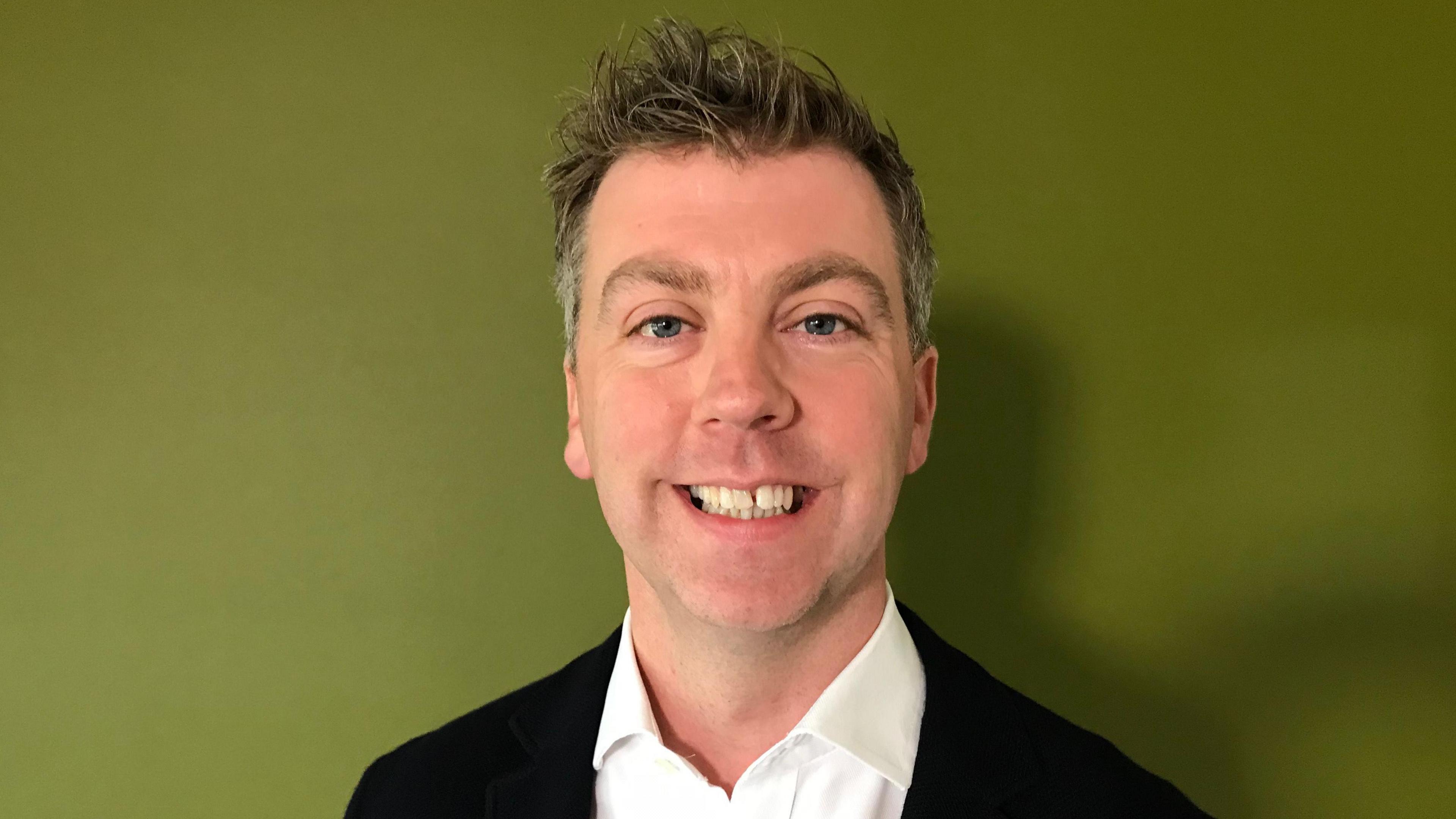 Nick Evans, Deputy Police and Crime Commissioner, smiling at the camera with an olive green wall behind him