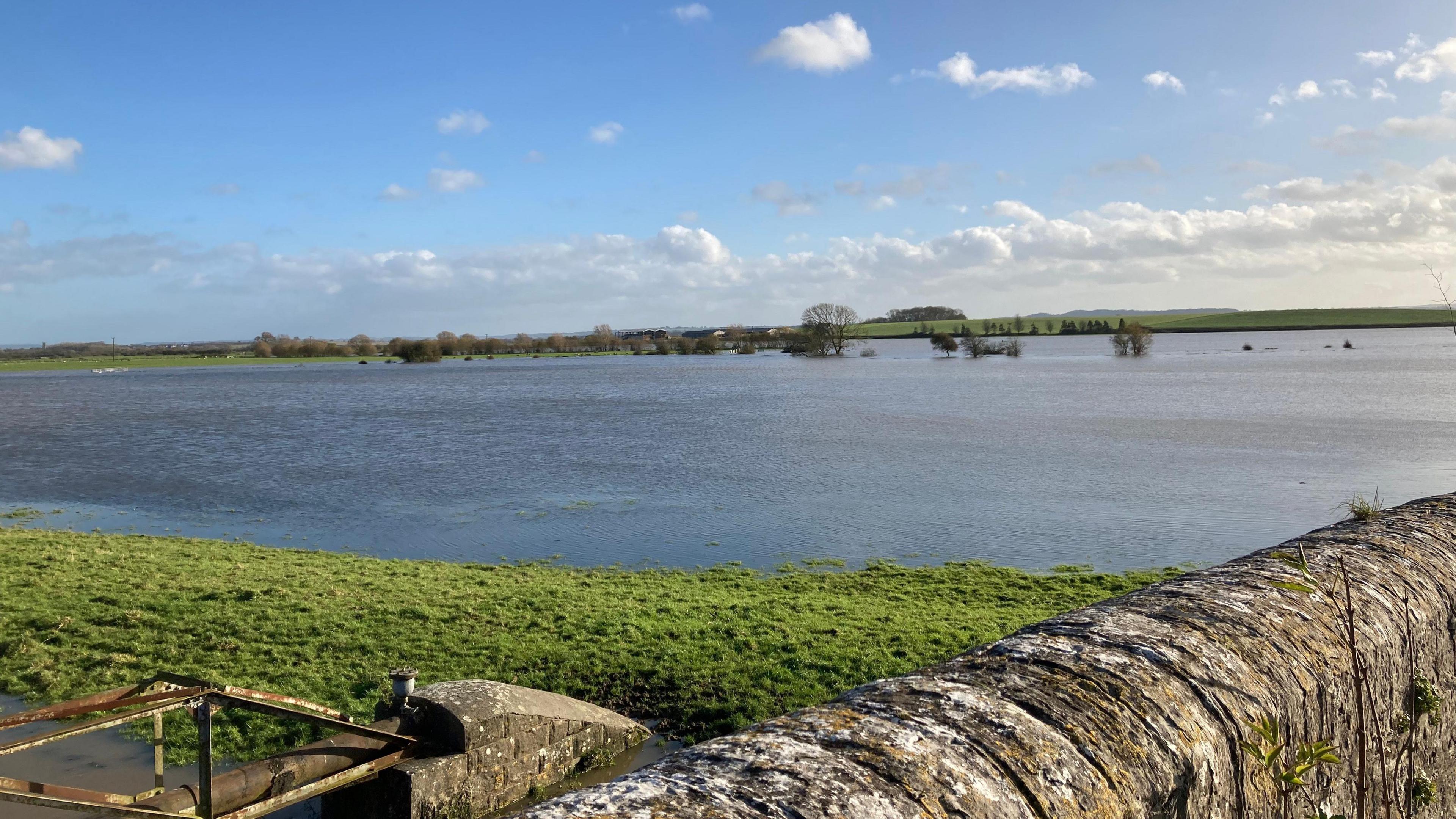 Field and road underwater on the Somerset Levels. A stone wall is visible in the foreground