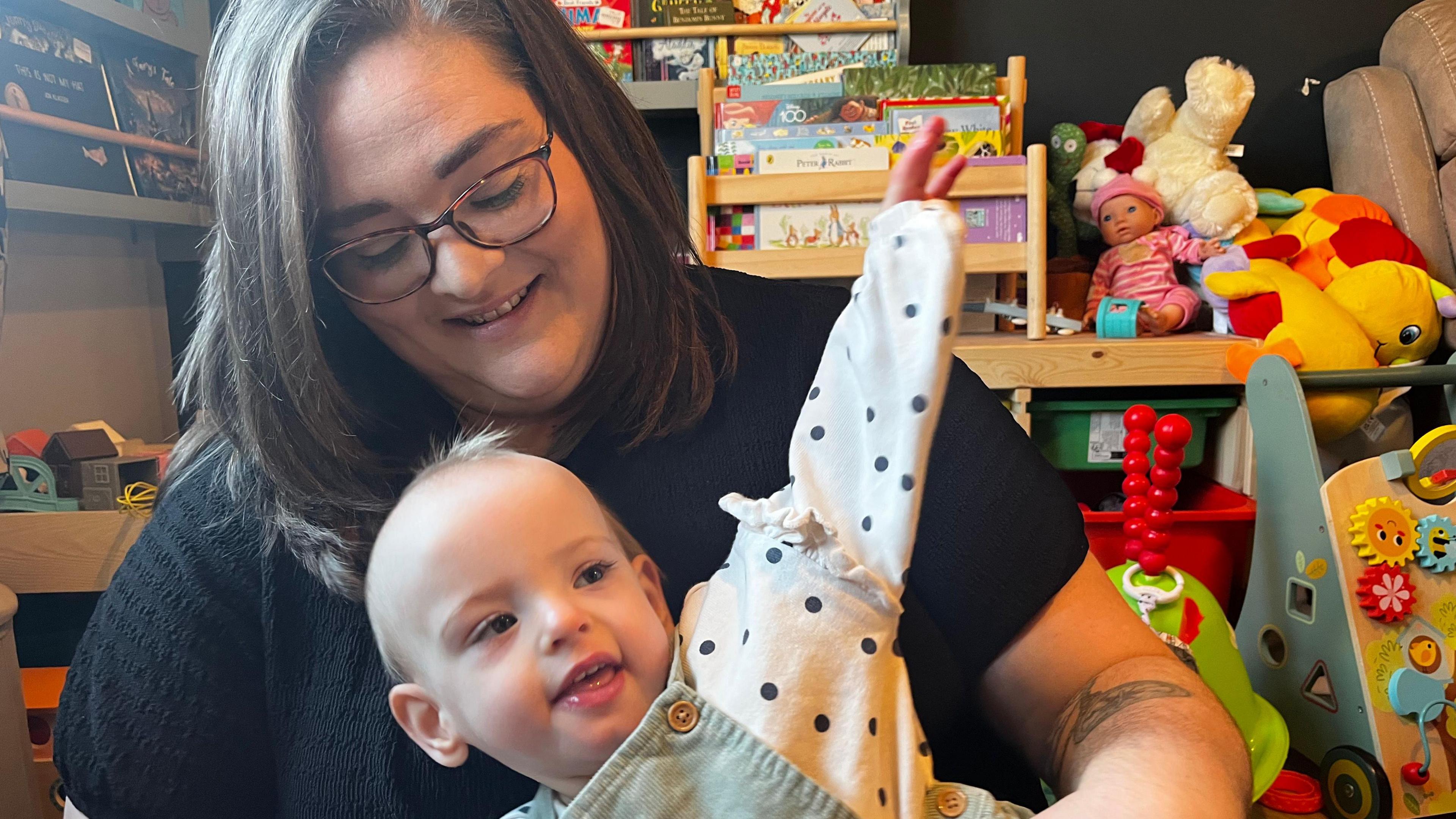 Wren wearing a green pinafore and white shirt with black dots sitting in Naomi's lap - wearing  black shirt 