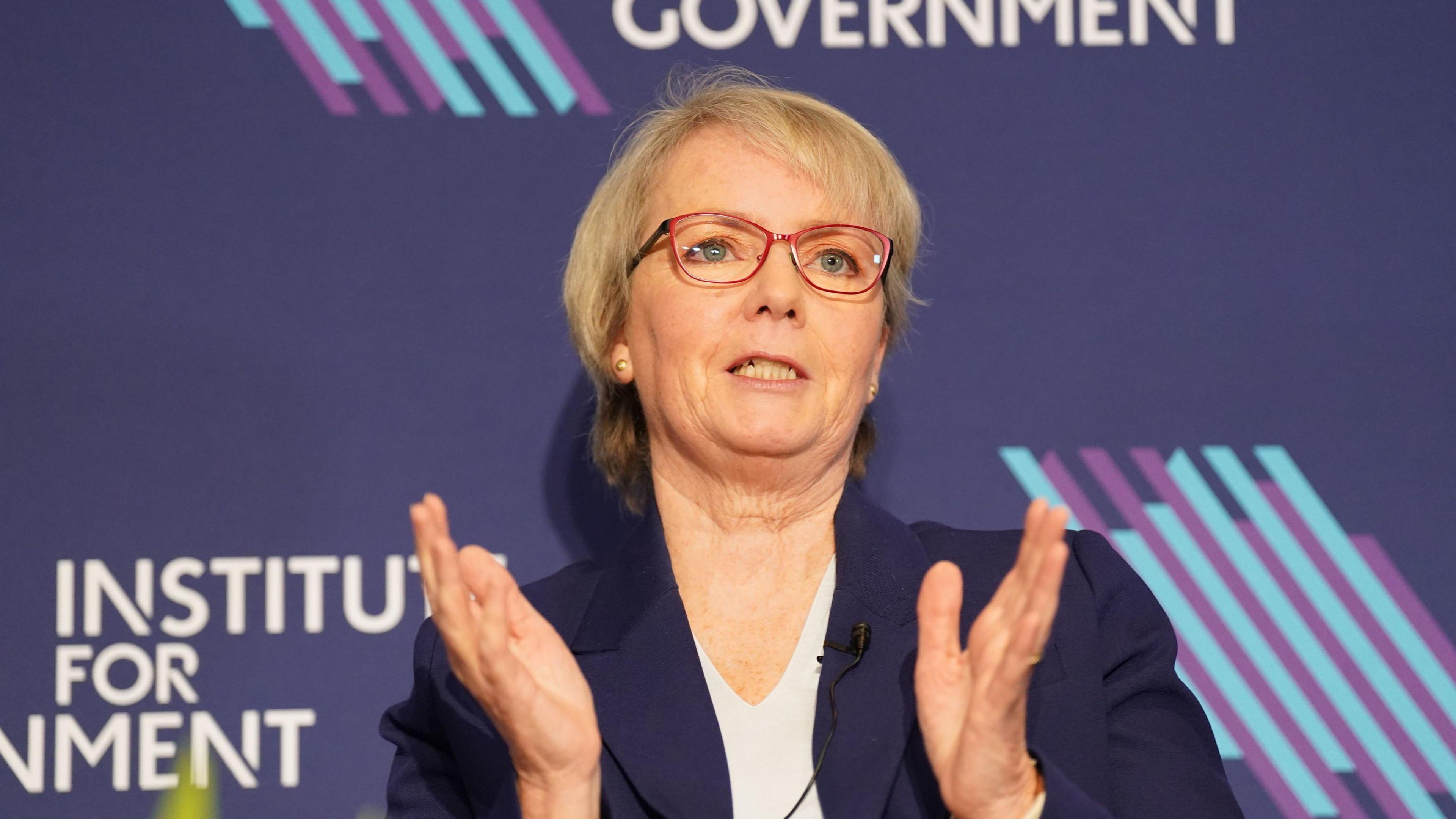 Karin Smyth with short blond hair wearing a blue jacket and clapping