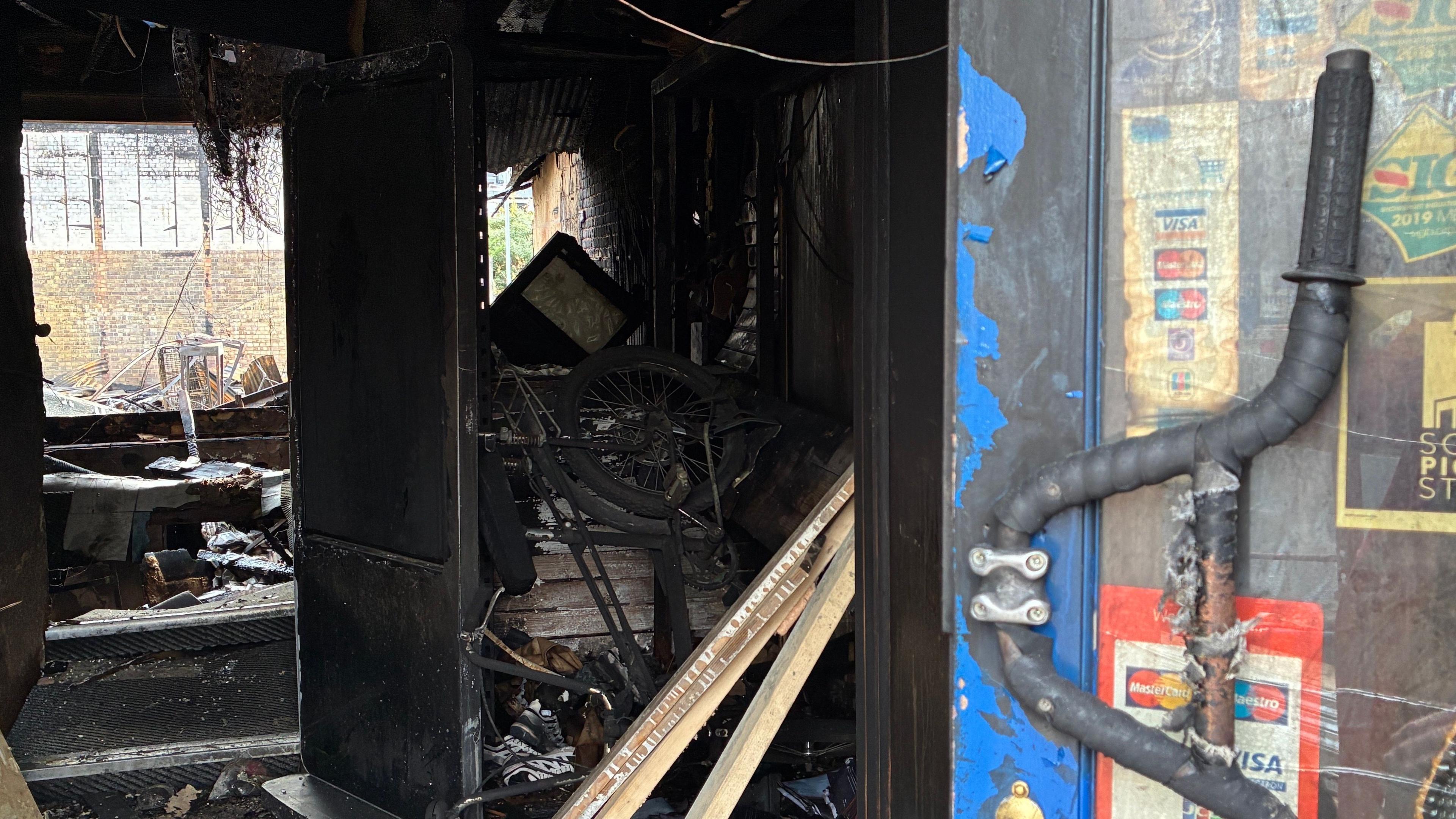 Bike handlebars are fixed to the front door of the shop, which is open to reveal blackened debris and a view straight through to the outside at the back