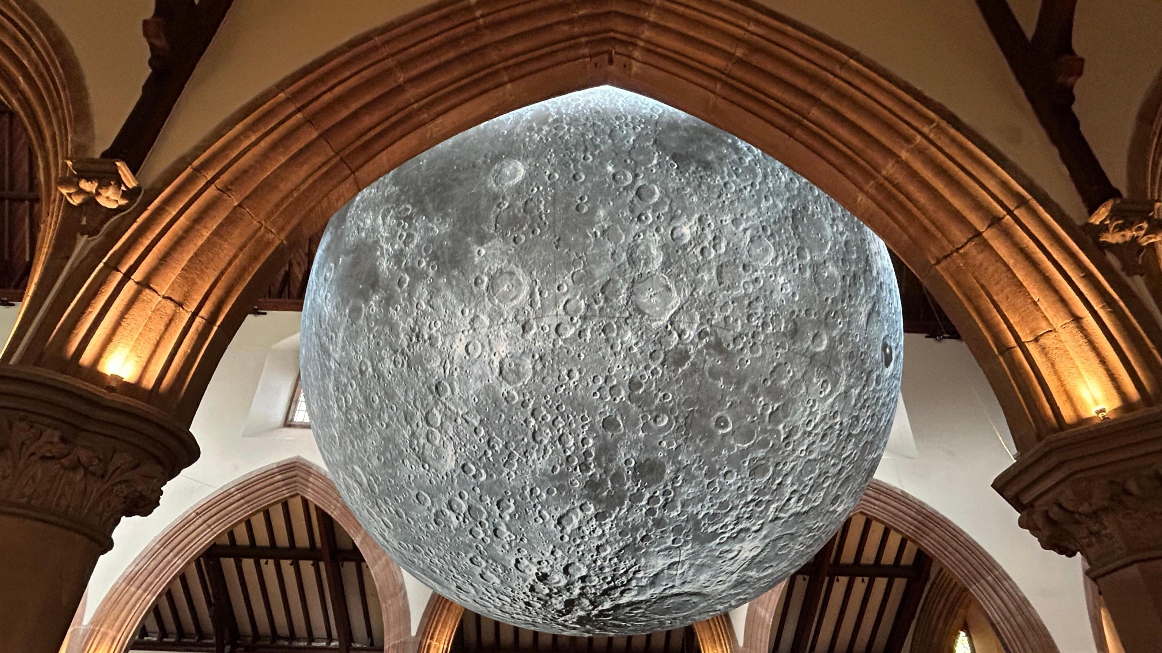 The sculpture of the moon from the side through the view of an arch in the cathedral.