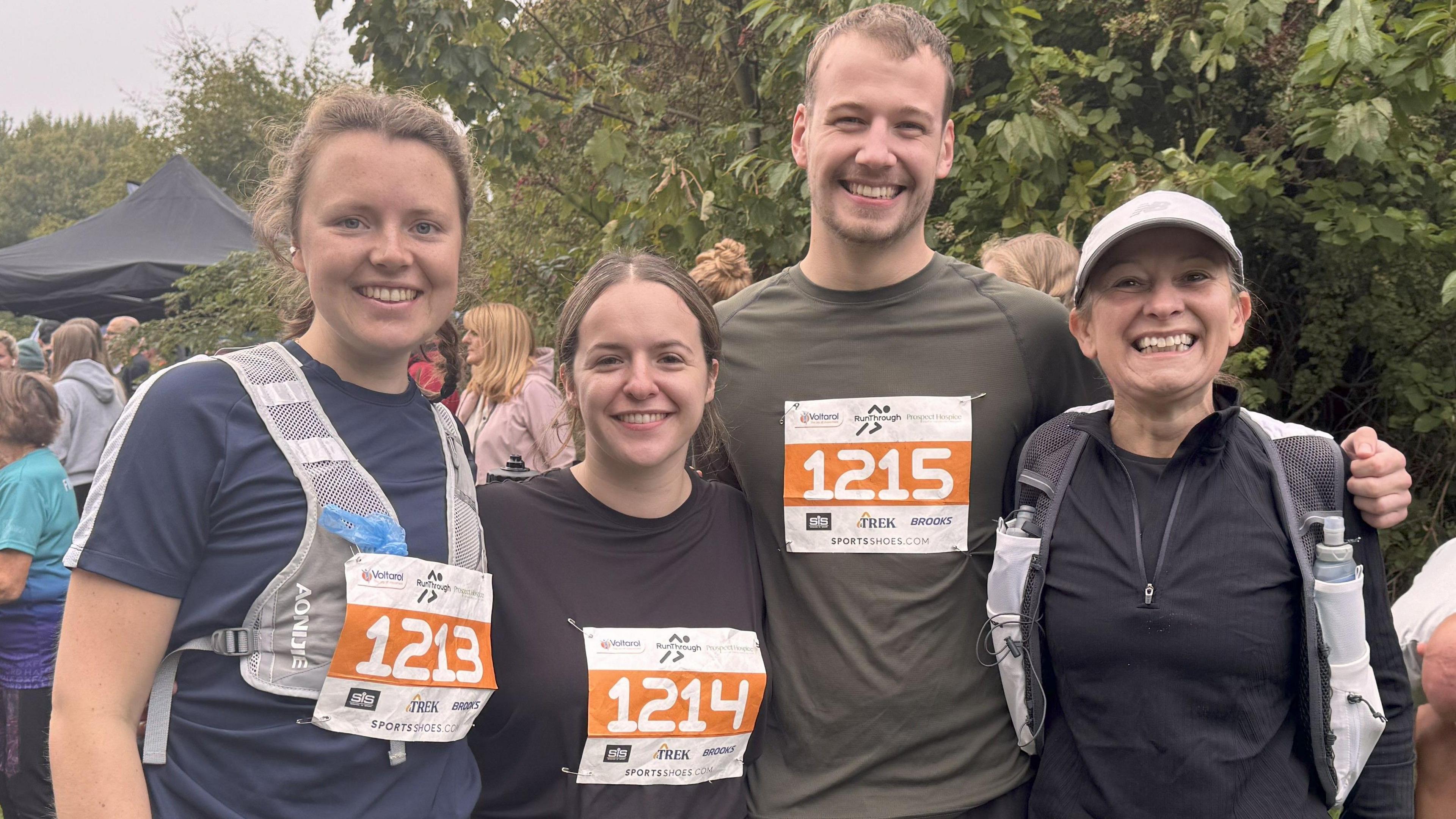 For people - three woman one man - smile at the camera. They are wearing running gear and have their marathon numbers on.