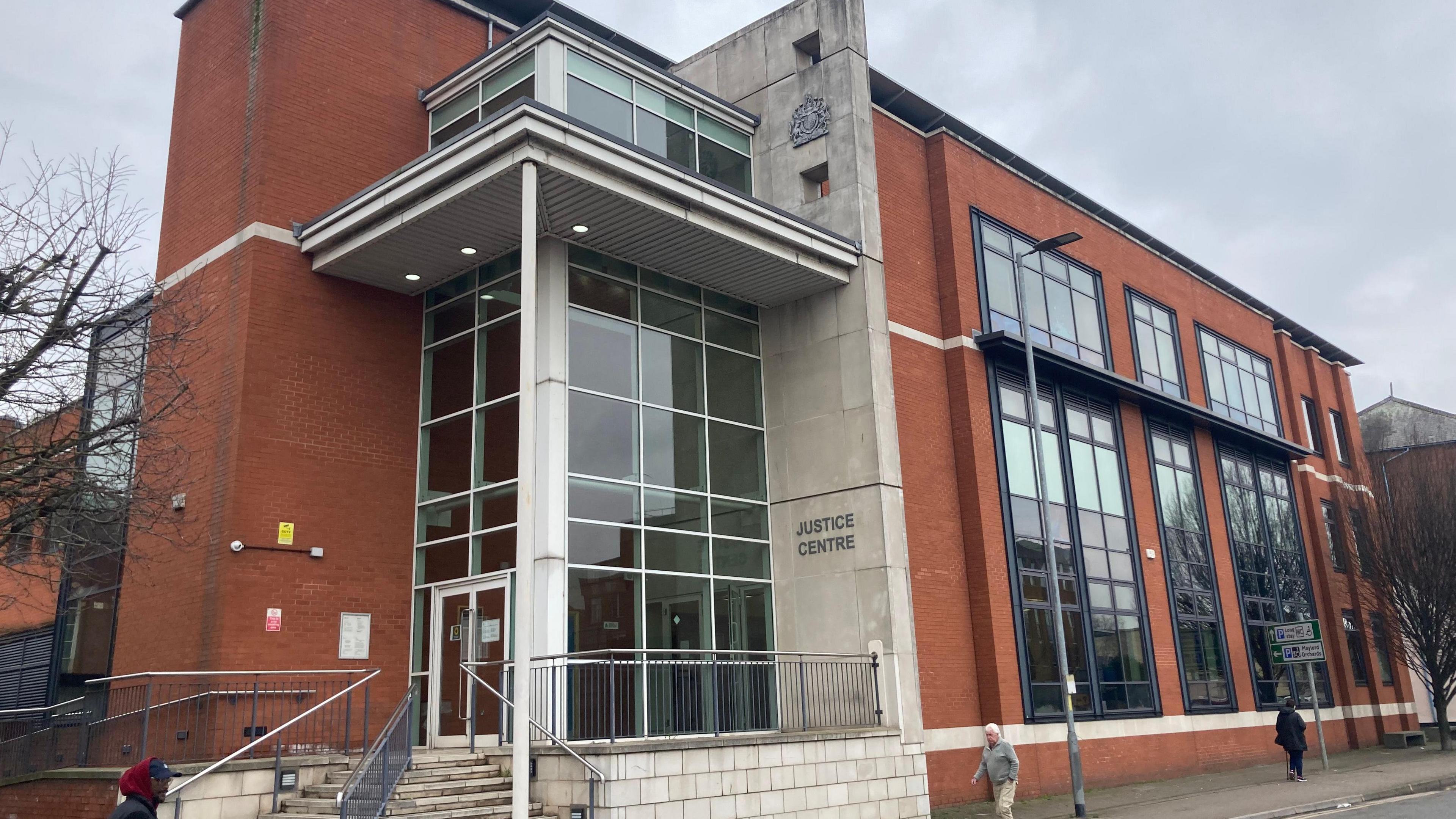 The outside of Warwick Crown Court, a modern building with large windows and steps lewading up to the entrance. People are walking past on the pavement.