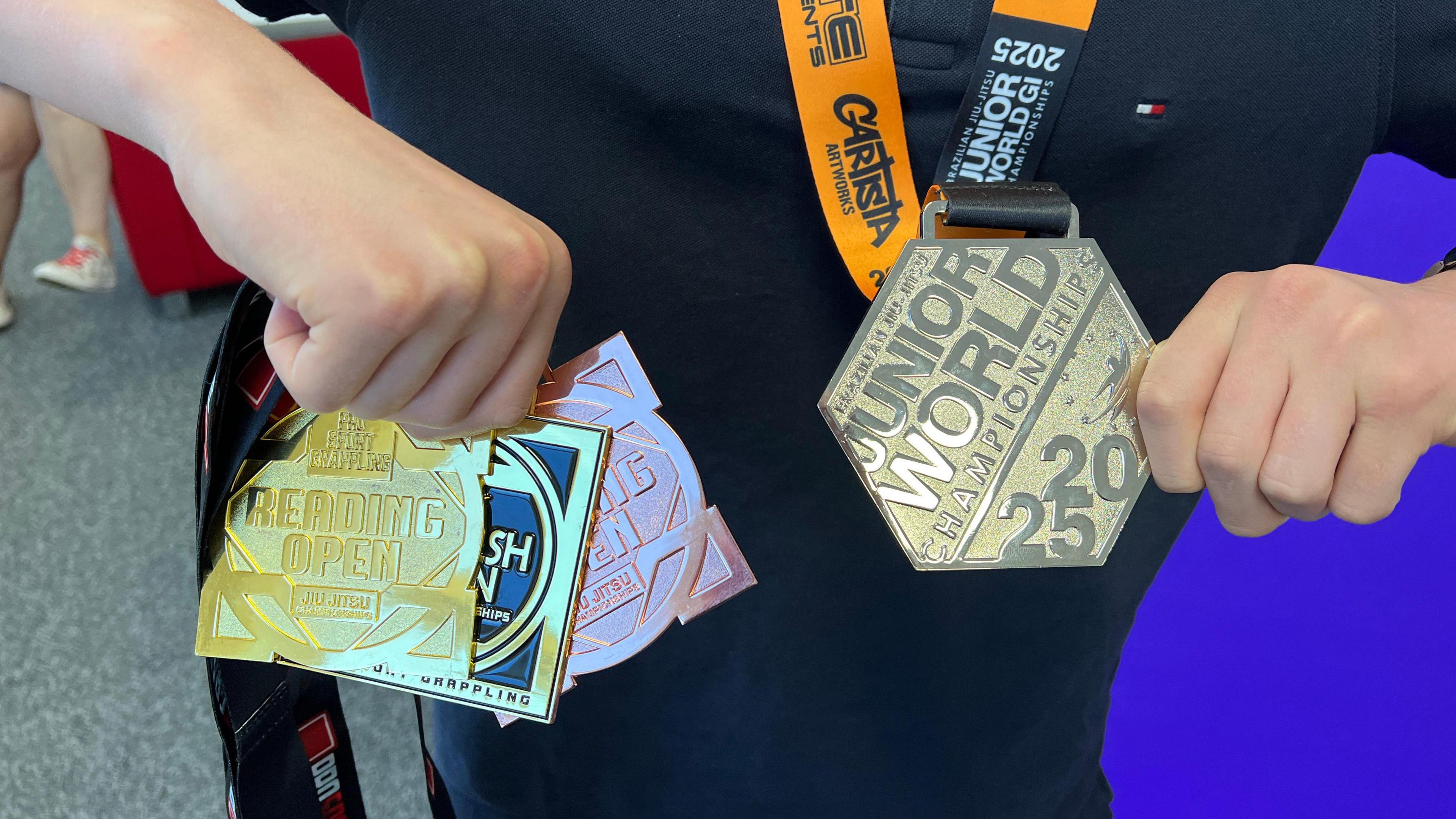 A close up shot of Roman's medal collection. He is holding three medals in his right hand. Two gold and one bronze. And in his left hand he is holding his silver medal.