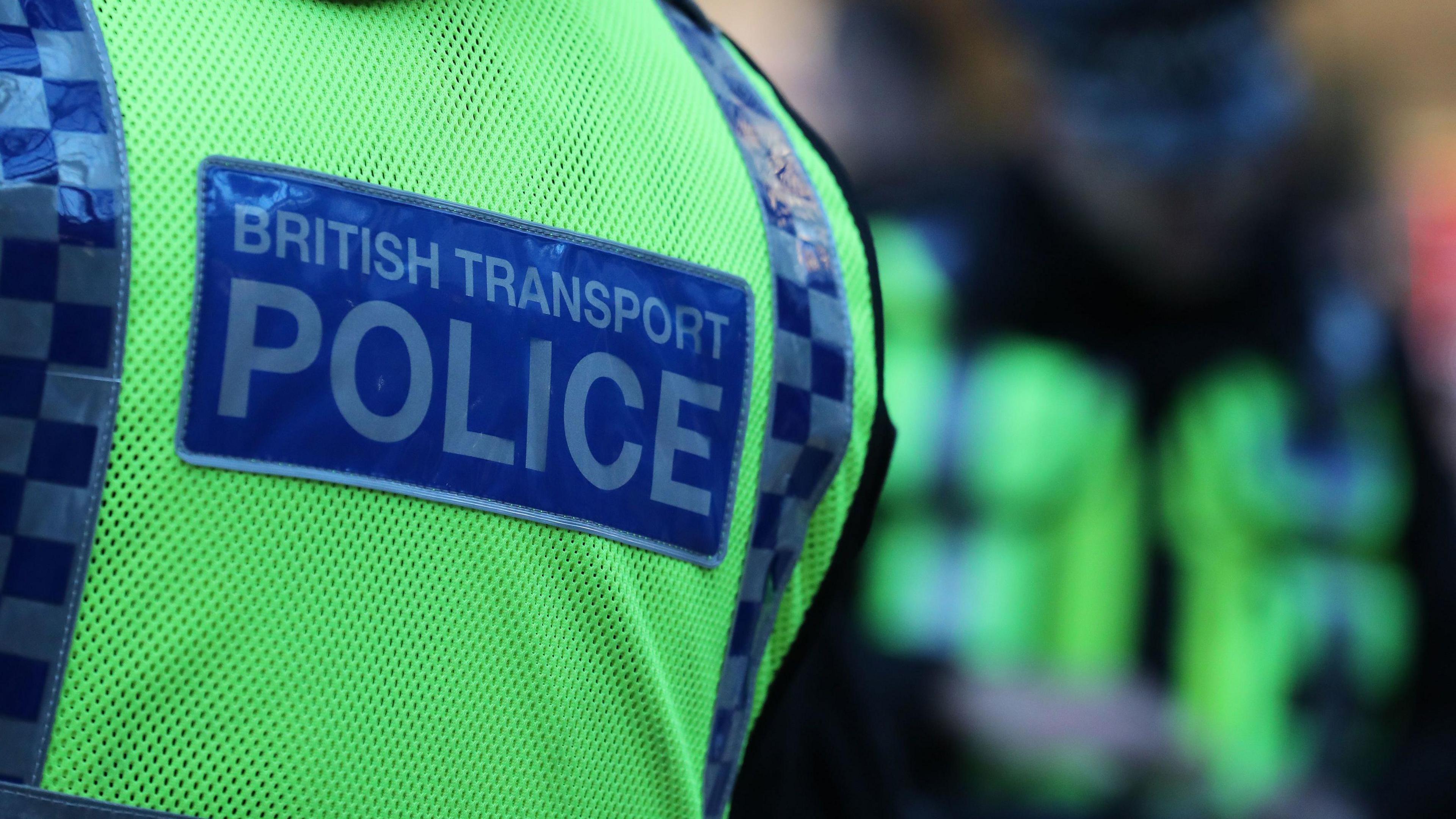 A close up image of a person's back. They are wearing a hi-vis vest which has a blue patch which says British Transport Police on it.