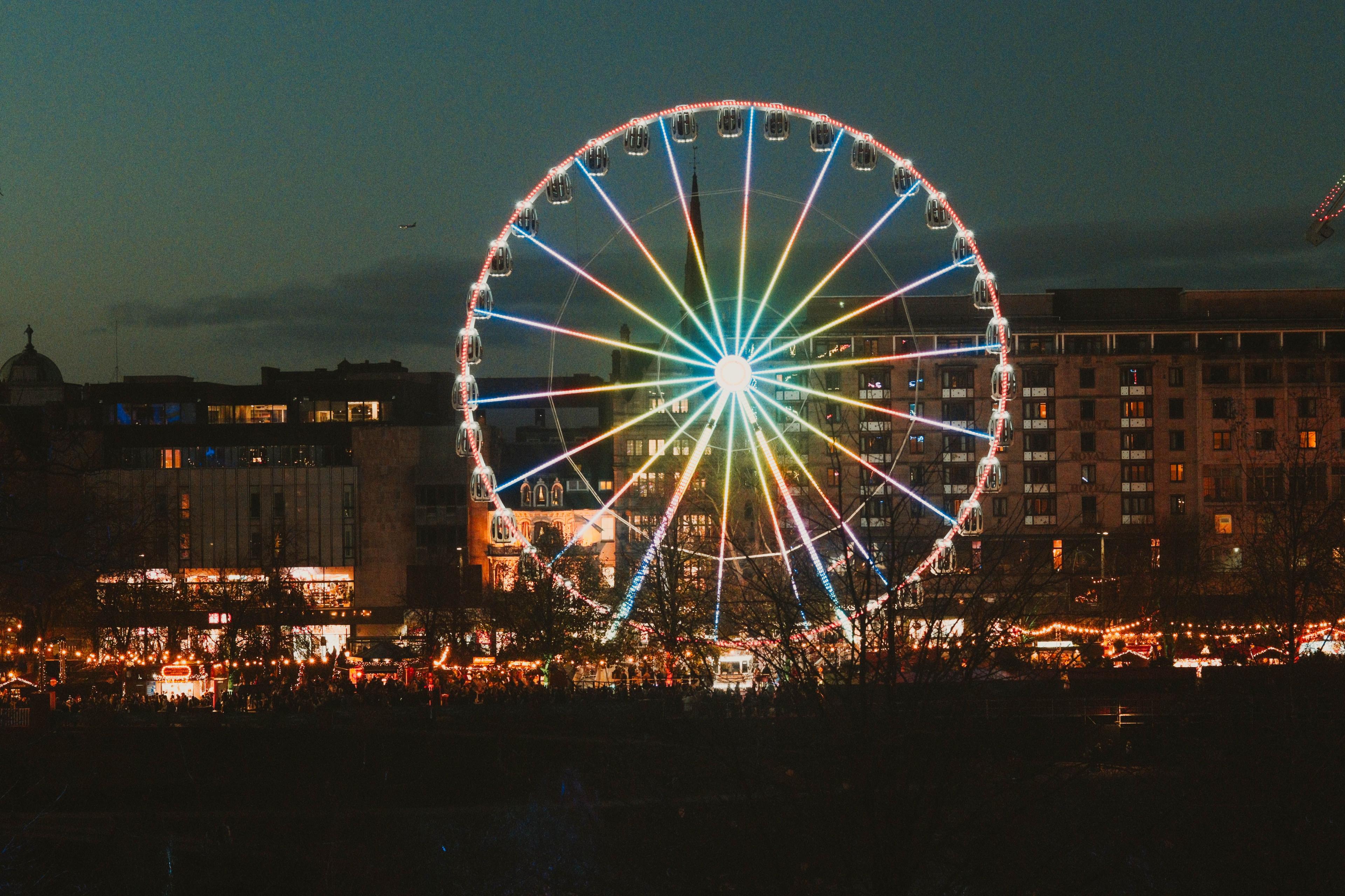 A ferris wheel at night lit up on a busy Edinburgh street