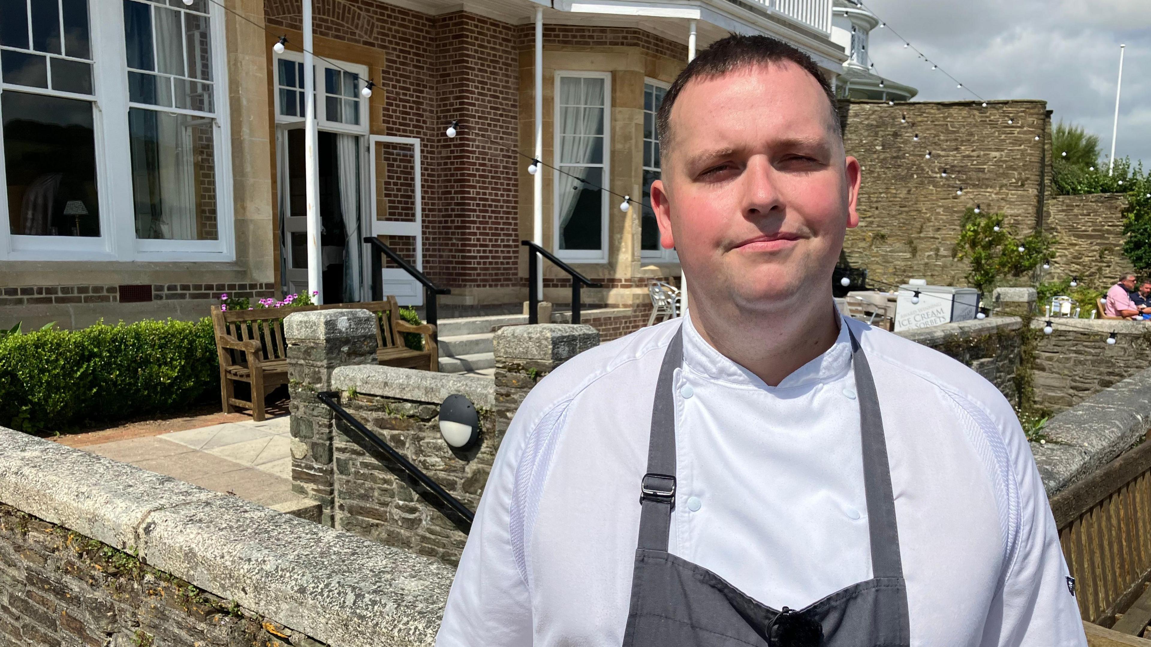 Jamie Rogers in a chef's apron, standing on a sunny restaurant terrace