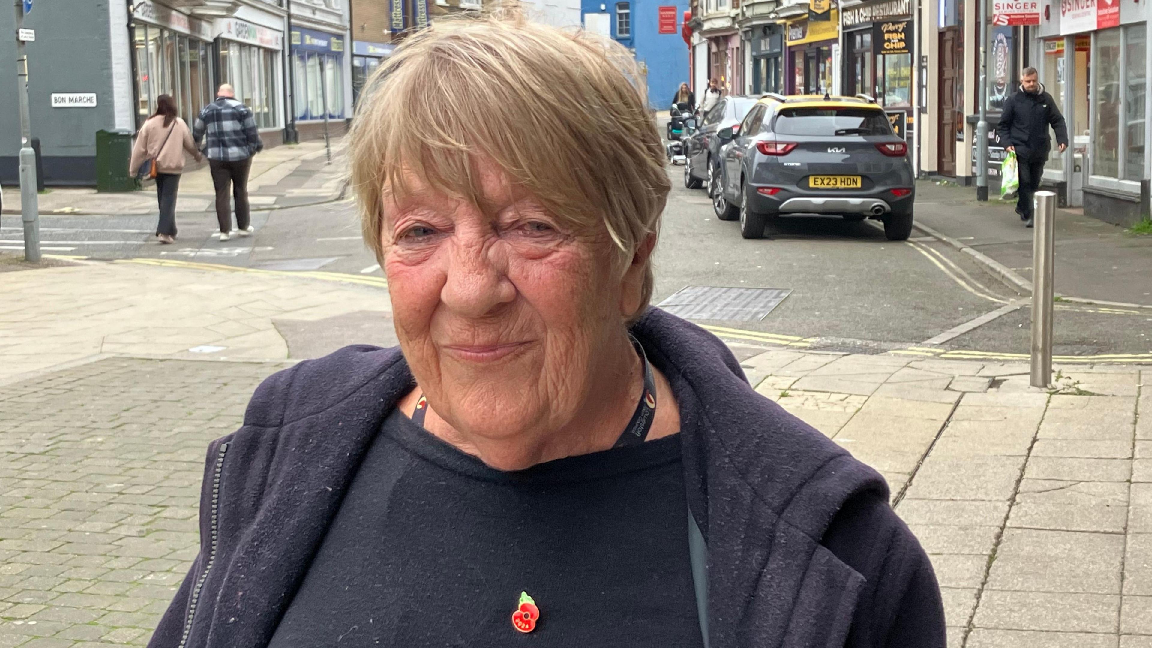 Town Councillor Wendy Brooks stands in a Lowestoft street wearing a blue coat over a black top  