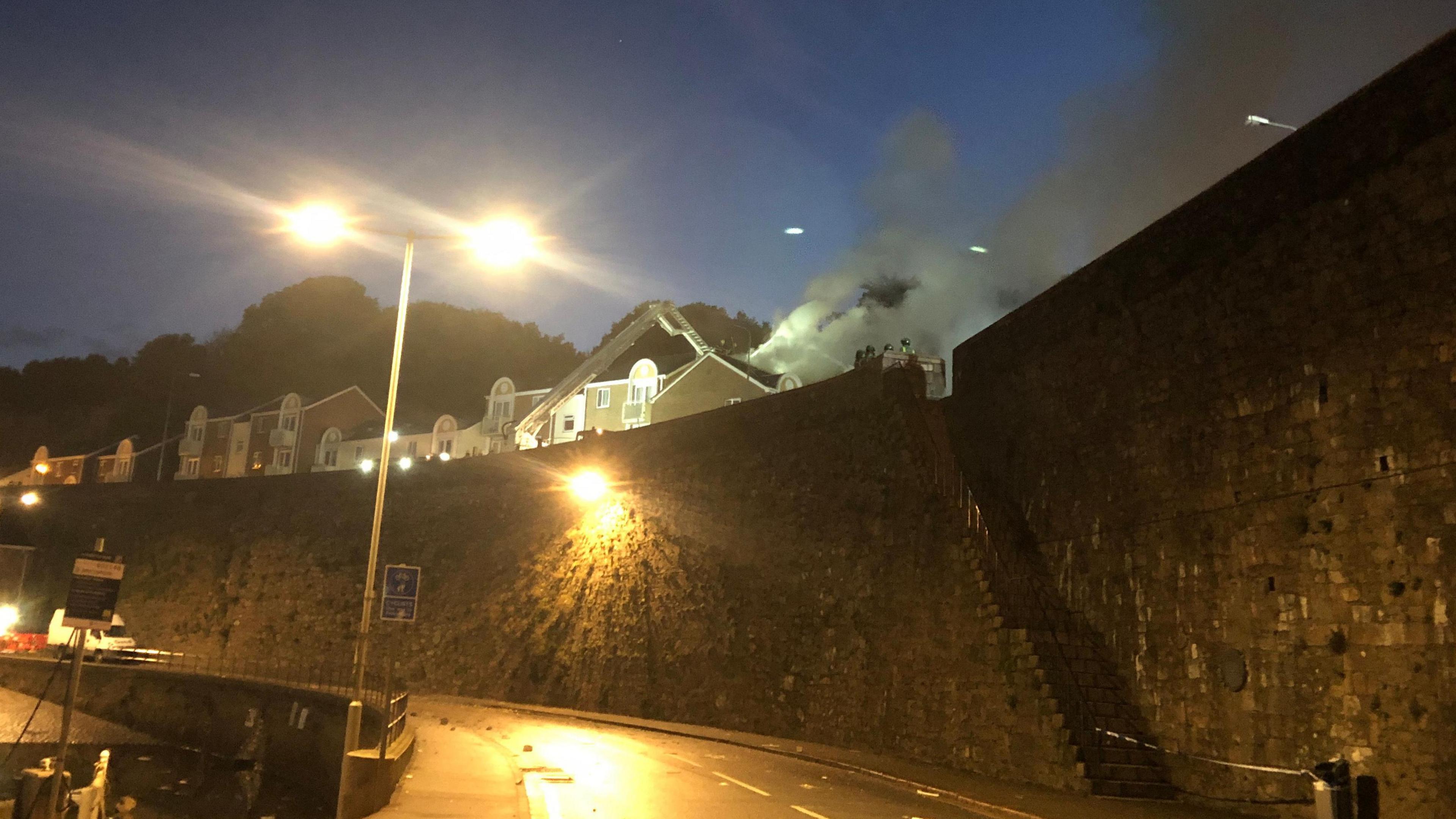 Smoke pours into the night sky in St Helier following an explosion at Haut du Mont. A fire engine is at the scene.