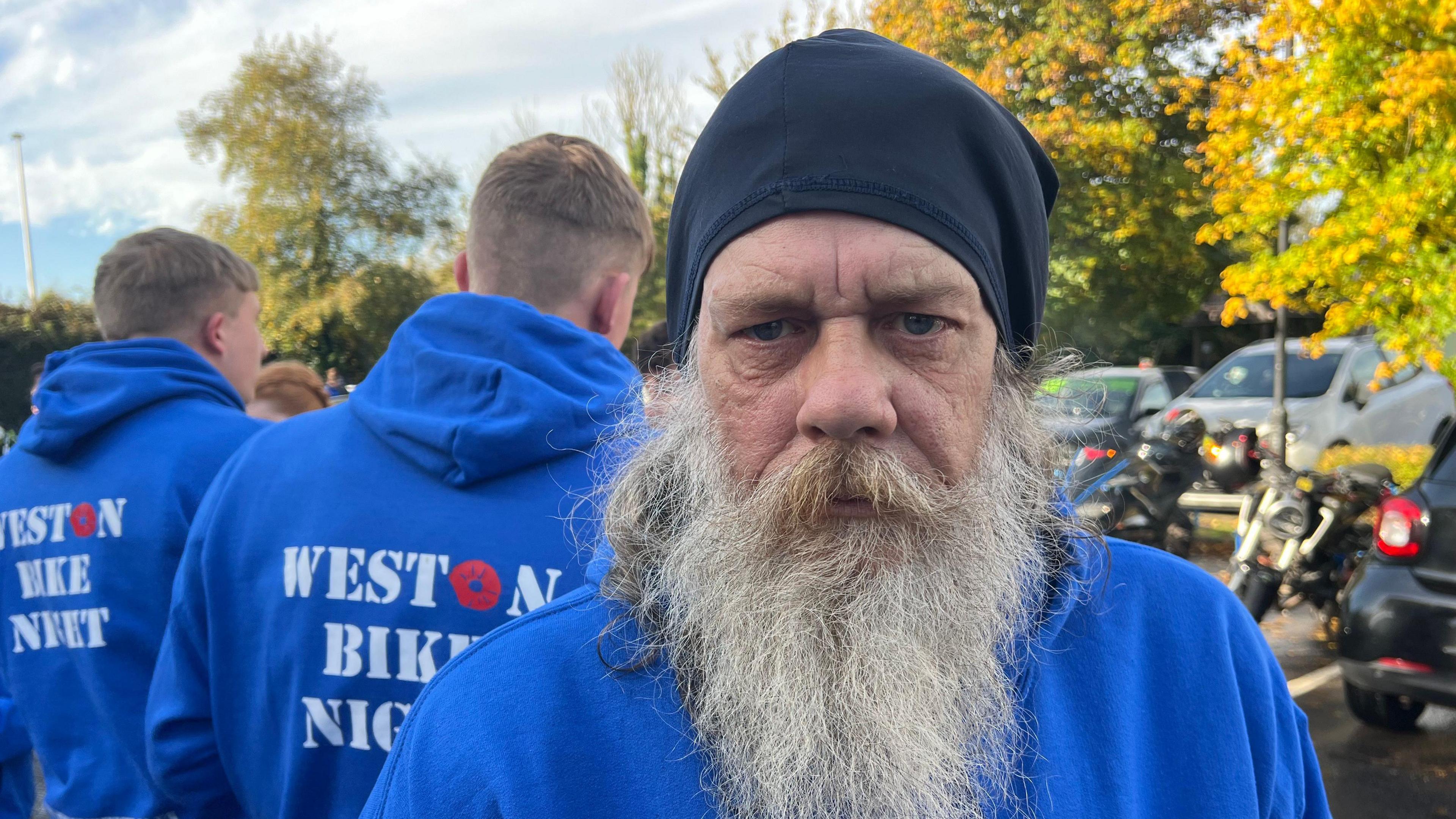 Mark Threadgold looking at the camera with funeral members in the background, all wearing a blue hoodie as tribute