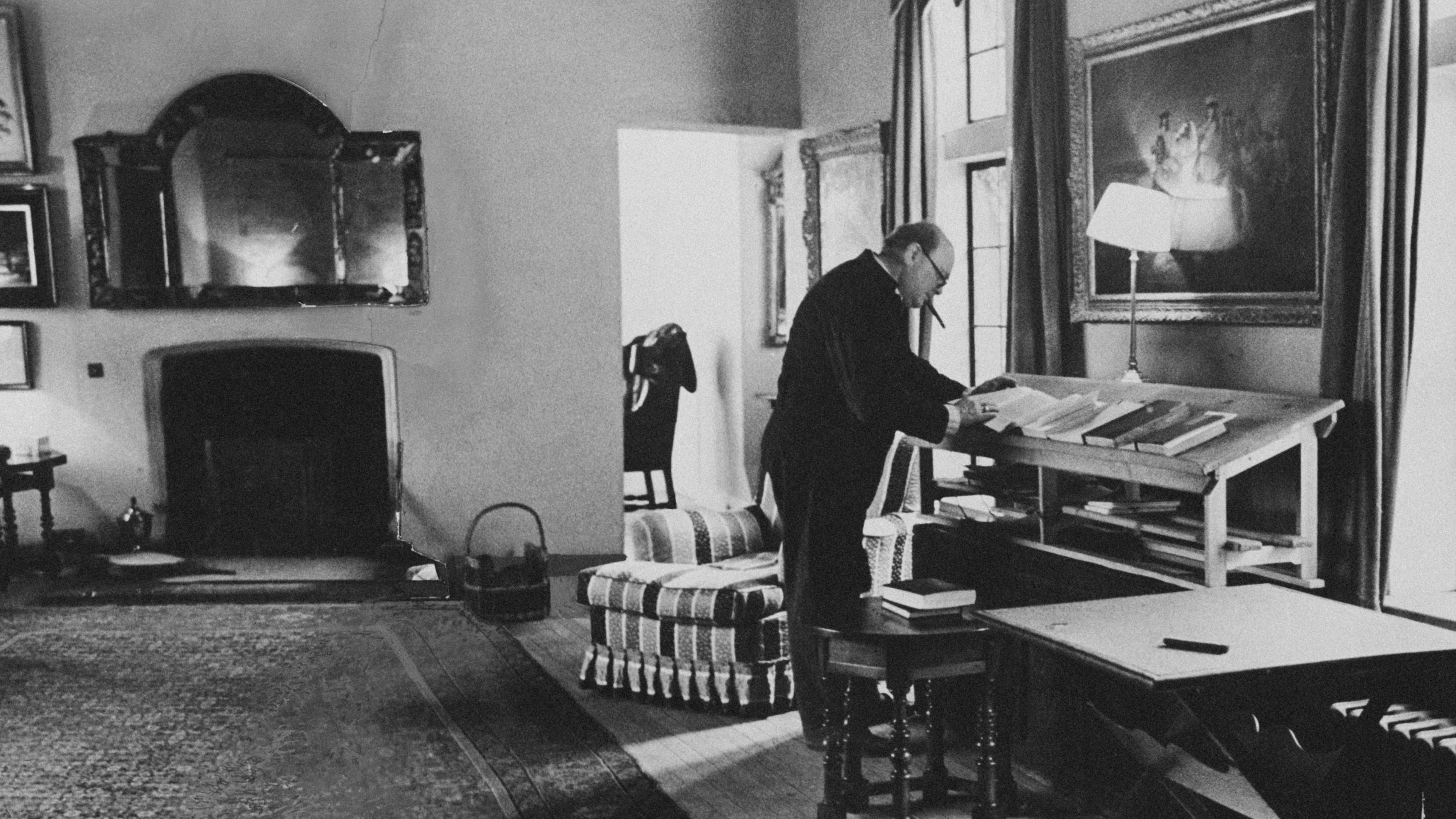 Sir Winston Churchill in his Chartwell home leaning over a magazine table and smoking a cigar