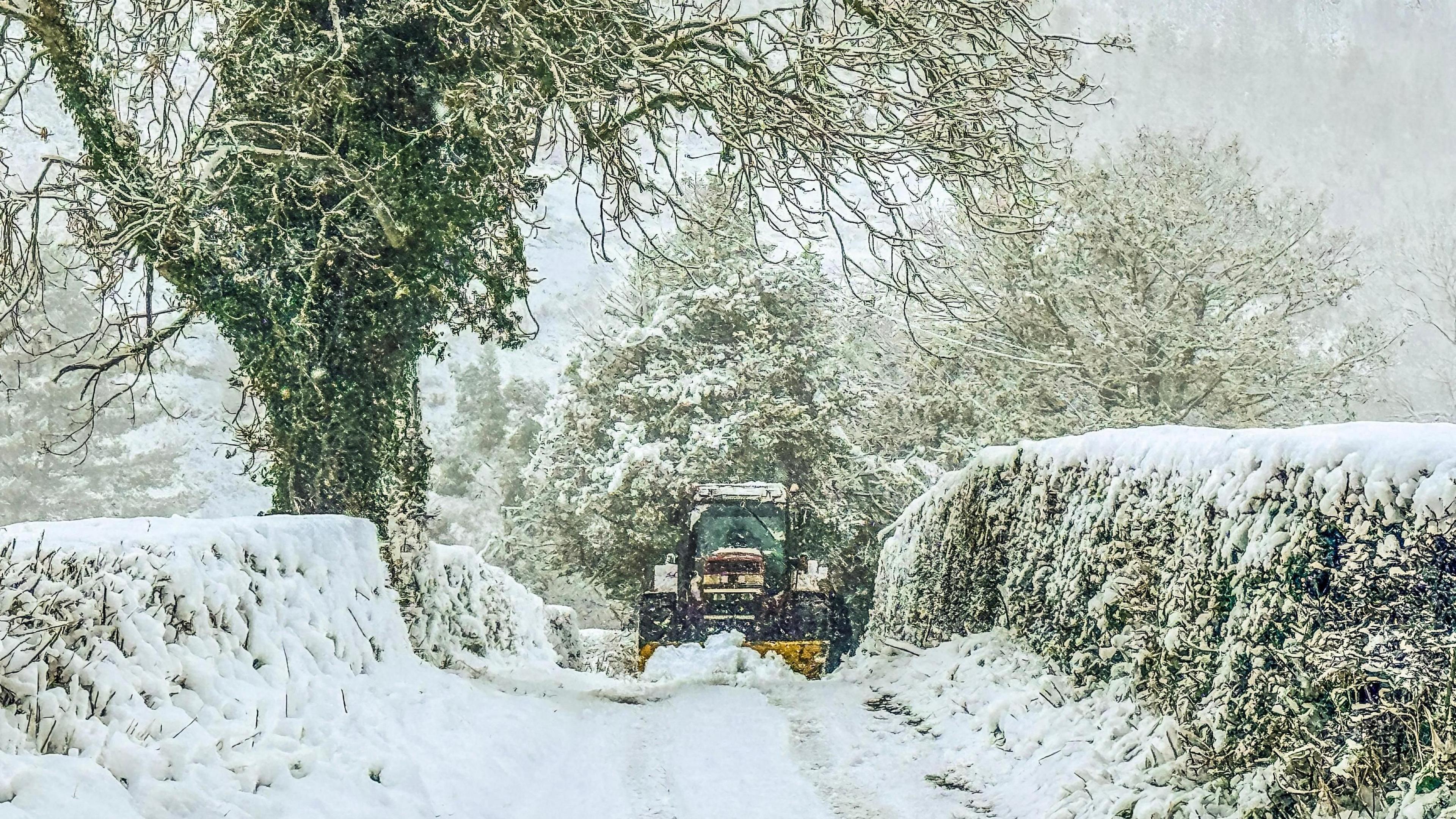 Tractor yn gyrru trwy'r eira ar lôn yn Llanfair, Dyffryn Clwyd