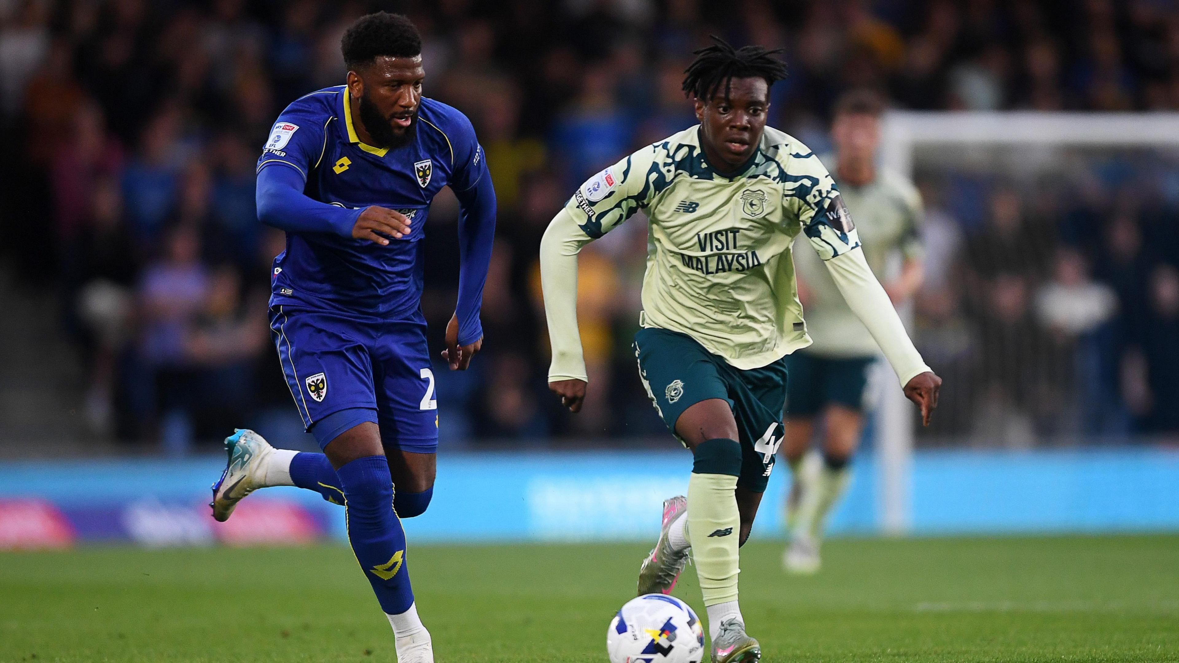 Ronan Kpakio of Cardiff City (R) is challenged by Myles Hippolyte of Wimbledon