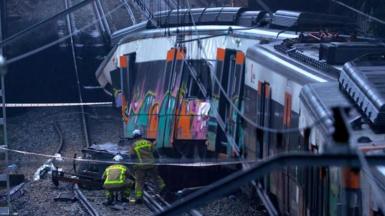 Firefighters are seen on a train track next to the derailed carriage of a commuter train near Barcelona