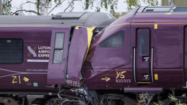 Two trains that have collided. One train is badly damaged. The driver's cab is crumpled and twisted.