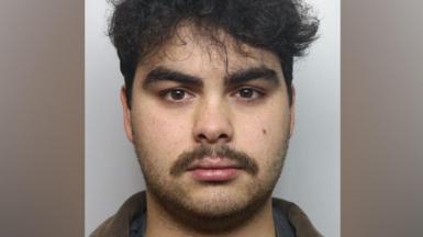 Kyran Smith, a man with black curly hair and a dark moustache, is pictured in a police mugshot. 