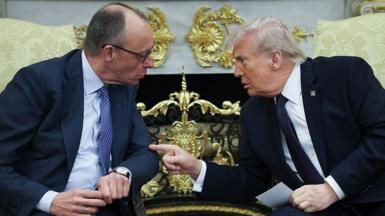 Trump and Merz speak in the Oval Office. They are seated and lean towards each other. Trump points a finger at Merz
