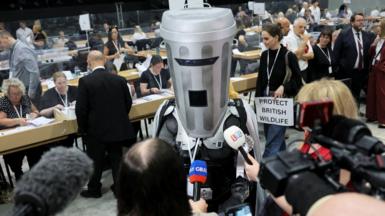 Count Binface, a man dressed as a bin with head covered, speaks to members of the press