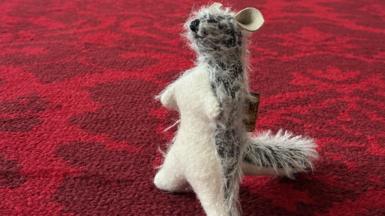 Roo on the carpet at Buckingham Palace - it's a teddy bear on that looks like the baby kangaroo character from Winnie-the-Pooh. It has scruffy grey and white fur with big ears and a long tail. He has a white underside