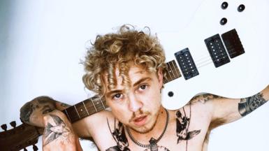 A photo of a topless man with a guitar 