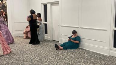 Women dressed in their finest outfits sitting on the floor scrolling on their phones