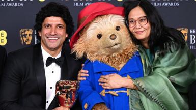 Indian film producer Farhan Akhtar (left), wearing a tuxedo over a white shirt, and filmmaker Lakshimipriya Devi, wearing a saree, pose with Britain's beloved Paddington Bear, wearing its signature blue duffle coat along with a red hat. 