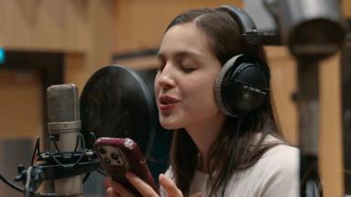 Olivia Rodrigo sings while reading lyrics from her phone