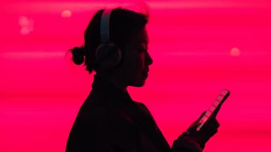 Woman in silhouette listening to music on smarphone in front of a bright pink background