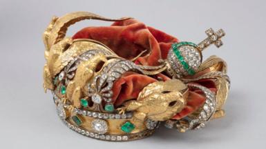 The crown of French Empress Eugenie - a gold crown featuring diamonds, emeralds and golden eagles and a red velvet covering. Its decorations can be seen crushed inwards 