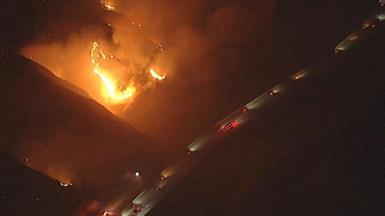 Aerial night time image of vehicles driving on a road close to orange wildfire flames.