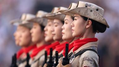 Soldiers line up looking solemnly ahead while wearing red neck bandanas and holding rifles to their chest during the parade in Beijing on Wednesday