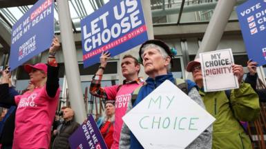 A group of protesters hold colourful pro-assisted dying signs