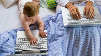 A baby and woman both place their hands on two laptops 