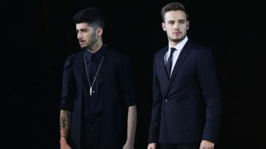 Zayne Malik and Liam Payne on stage with a black backdrop and both wearing black suits