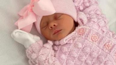 Thea Wilson dressed in a pink cardigan and hat, lying on a white sheet.