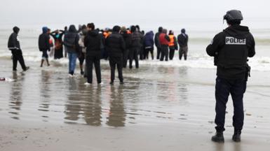 A police officer looks out to sea as a group of people wearing inflatable jackets stand in shallow water in Gravelines earlier this month.