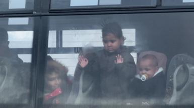 Three small children in a bus. One child has their hands pressed against the window