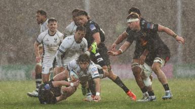 Bernhard Janse van Rensburg powers forward in a rainstorm as various Bristol Bears and Exeter Chiefs players look on.