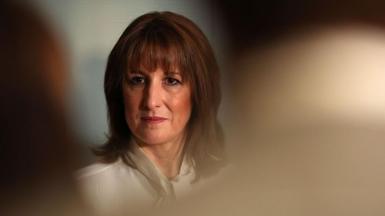 Rachel Reeves, dressed in a white blouse, can be seen in focus between the heads of an audience