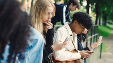 Stock photo shows teens outside looking at phones