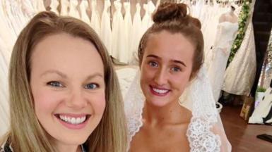 Emily Grant has long blonde hair and wears a zebra tolp and blakc tgrousers while Venezuela Fury is in her wedding dress