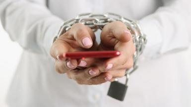 A woman's chained hand holds a red smartphone