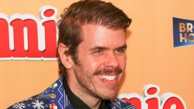 Perez Hilton smiles while attending an event in Hollywood in November 2022. He is wearing a vibrant blue suit with a bold pattern featuring snow flakes and characters from Super Mario. 
