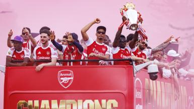 Bukayo Saka of Arsenal (R) lifts the English Premier League trophy as he and teammates ride an open-top bus during Arsenal Champions Parade in north London